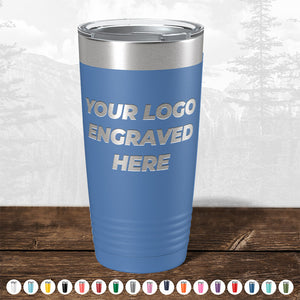 A blue Kodiak Coolers Custom Tumbler with a silver lid sits on wood, featuring "YOUR LOGO ENGRAVED HERE." Ideal as a branded gift, this tumbler is available in various colors. No setup fees; $200 minimal order for logo or design engraving.