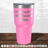A pink insulated tumbler labeled "Your Logo Engraved Here" is displayed on a wooden surface with a mountain backdrop. Kodiak Coolers' custom tumblers are ideal corporate gifts, available in various colors with bulk wholesale pricing and no setup fees.