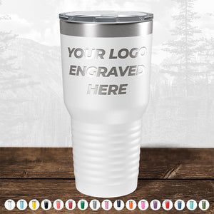 **Product Description:**
The white insulated tumbler from Kodiak Coolers features the custom engraving "YOUR LOGO ENGRAVED HERE" and is showcased on a wooden surface. Below, an array of colorful tumbler caps are displayed, against a subtle outdoor landscape backdrop. This makes it an ideal promotional gift for companies interested in personalized logos on custom mugs. Take advantage of our HUGE LABOR DAY SALE—ENDS TODAY!