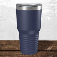 A navy blue Kodiak Coolers 30 oz tumbler, laser engraved with Wisconsin Green Bay Bulldogs, sits on a wooden surface with a mountain backdrop, featuring a stainless steel rim and clear lid.