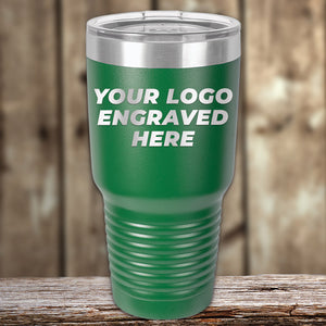 A green Kodiak Coolers Custom Tumbler with clear lid and engraved logo sits on wood, ideal as a personalized mug for promotional gifts. No setup fees; $200 minimal order.