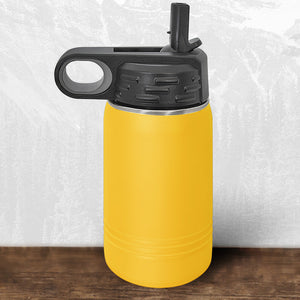A Kodiak Coolers Wisconsin Luxemburg Casco Spartans 12 oz yellow water bottle with a black flip top straw lid and carrying handle is displayed on a wooden surface against a light patterned background.