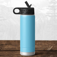 A Kodiak Coolers 20 oz water bottle with flip top straw and carrying handle, laser engraved with the Wisconsin Green Bay Bulldogs logo, rests on a wooden surface against a blurred mountain background.