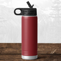 A Kodiak Coolers 20 oz water bottle with flip top straw, featuring a laser-engraved Wisconsin Luxemburg Casco Spartans design, stands on wood before a blurred mountain—ideal drinkware for Spartans fans.