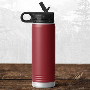 A Kodiak Coolers 20 oz water bottle with flip top straw, featuring a laser-engraved Wisconsin Luxemburg Casco Spartans design, stands on wood before a blurred mountain—ideal drinkware for Spartans fans.