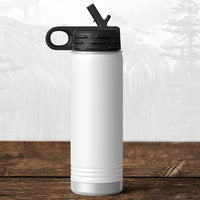 A Kodiak Coolers Wisconsin Green Bay Bulldogs 20 oz water bottle with a flip top straw lid features a laser-engraved design and stands on a wooden surface against a blurred mountain background.
