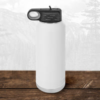 A white 32 oz Kodiak Coolers water bottle with a black flip top straw lid, laser engraved with the Wisconsin Green Bay Bulldogs logo, sits on wood with mountains in the background.