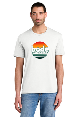 A man wears the 2026 Bode Summer Bootcamp OG Logo Unisex T-Shirt DM130 Tri Blend by Printify, featuring a white tri-blend fabric and a sunset graphic with "bode SUMMER CAMP" on the front, as he stands looking at the camera.