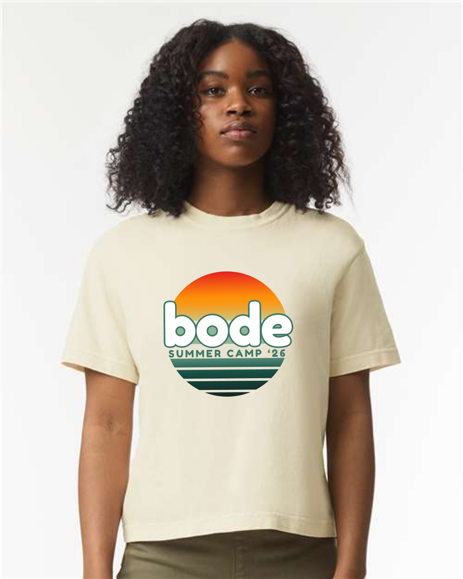 A person wearing the designerapp BODE Summer Camp 2026 "OG Logo" Women's Crop Top (Comfort Colors 3023CL), a boxy fit light tee featuring a sunset graphic and "bode SUMMER CAMP '26" on the front.