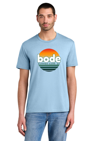 A man wearing a Printify 2026 Bode Summer Bootcamp OG Logo Unisex Tri Blend T-Shirt in light blue, featuring a sunset graphic and "bode SUMMER CAMP '23" on the front.