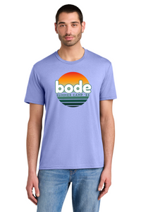 A man wears a Printify 2026 Bode Summer Bootcamp OG Logo Unisex T-Shirt DM130 Tri Blend in light purple, featuring a sunset graphic and "bode SUMMER CAMP '23" on the front, made of breathable tri-blend fabric.