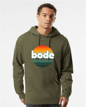 A person wears a Printify OG Logo Hoodie Sweatshirt (2026 Bode Summer Bootcamp, Unisex Independent Trading Co. SS4500) in olive green, featuring a sunset "bode summer camp 2024" logo on the front.