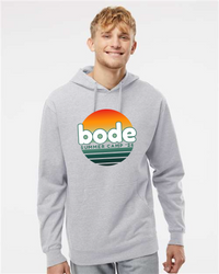 A young man wears a gray Printify 2026 Bode Summer Bootcamp OG Logo Hoodie Sweatshirt by Independent Trading Co. SS4500, featuring a sunset graphic on the front.
