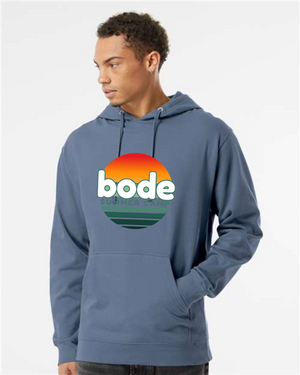 A person wears a Printify 2026 Bode Summer Bootcamp — OG Logo Hoodie Sweatshirt (Unisex Independent Trading Co. SS4500), featuring a sunset logo and cozy cotton-poly fleece with an adjustable hood, posed against a plain background.