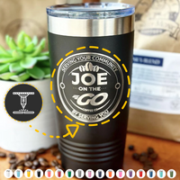 A Kodiak Coolers custom tumbler, laser engraved for added personalization, sits on a wooden surface surrounded by coffee beans, with a blurred background suggesting a cozy café setting.