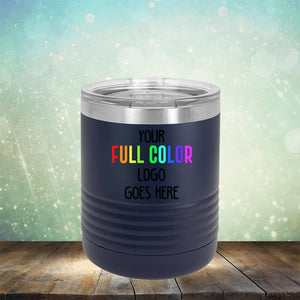 A black travel tumbler on a wooden surface in front of a light and bokeh background displays the text "Your Full Color Logo Goes Here." These Kodiak Coolers Custom UV Printed Drinkware - Single Side Printing Included in Price are perfect for showcasing your brand on the go.