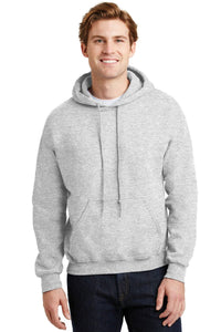 A person wears a light gray Gildan Heavy Blend™ Hooded Sweatshirt 18500 (Pack of 36, with custom screen printed logo) and dark jeans, standing forward, smiling, hands at their sides.