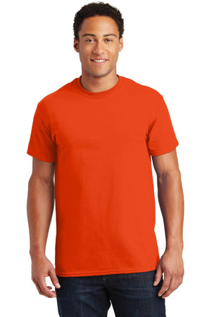 Wearing a vibrant orange Gildan - 100% US Cotton T-Shirt 2000 and dark jeans, a person stands against a white background, facing the camera.
