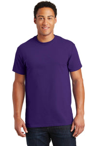 A person wearing a purple Gildan - 100% US Cotton T-Shirt 2000, crafted entirely from US cotton, alongside dark jeans, is standing and smiling against a white background, ideal for promotional materials.