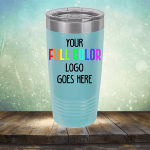 A light blue insulated tumbler with a lid is placed on a wooden surface. It has the text "YOUR FULL COLOR LOGO GOES HERE" in different colors against a blurred background with light spots, showcasing the perfect spot for Kodiak Coolers Custom UV Printed Drinkware - Single Side Printing Included in Price.