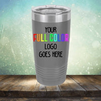 A grey Kodiak Coolers Custom UV Printed Drinkware - Single Side Printing Included in Price with the text "Your full color logo goes here" displayed on its surface, placed on a wooden surface against a blurred background. Perfect for those seeking customized tumblers for their brand or event.
