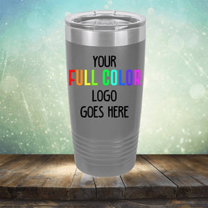 A grey Kodiak Coolers Custom UV Printed Drinkware - Single Side Printing Included in Price with the text "Your full color logo goes here" displayed on its surface, placed on a wooden surface against a blurred background. Perfect for those seeking customized tumblers for their brand or event.