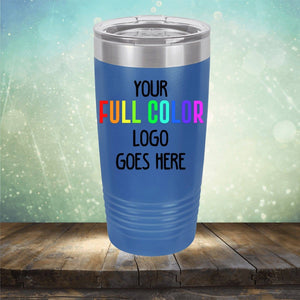 A blue tumbler with a stainless steel lid rests on a wooden surface with a blurred background. The text on the tumbler reads, "Your full color logo goes here" in various colors. Perfect for those seeking customized tumblers, it adds personalized flair to your drinkware collection. This is the Custom UV Printed Drinkware - Single Side Printing Included in Price by Kodiak Coolers.