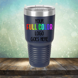 A stainless steel tumbler with a black exterior features the text "YOUR FULL COLOR LOGO GOES HERE" in white, red, orange, yellow, green, and purple. This sleek example of Custom UV Printed Drinkware - Single Side Printing Included in Price by Kodiak Coolers is placed on a wooden surface against a gradient background.