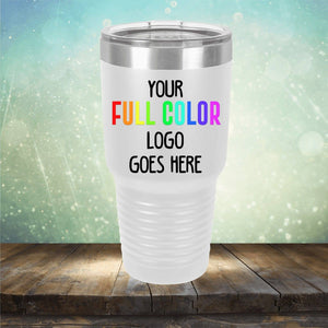 A white travel tumbler with the text "Your Full Color Logo Goes Here" printed on it, placed on a wooden surface against a blurred, light-colored bokeh background. These Custom UV Printed Drinkware - Single Side Printing Included in Price from Kodiak Coolers make for perfect personalized coffee mugs or engraved wine cups for any occasion.