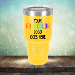 A yellow insulated tumbler with a metal lid rests on a wooden surface. The tumbler has a text placeholder that says, "Custom UV Printed Drinkware - ONE TIME SPECIAL OFFER by Kodiak Coolers." The background features a bokeh light effect, making it perfect for custom engraving.
