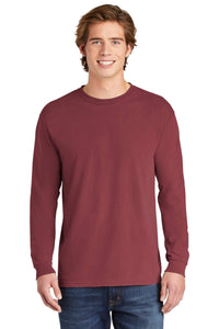 A young man, smiling at the camera, stands facing forward wearing blue jeans and a Comfort Colors Heavyweight Ring Spun Long Sleeve T-Shirt 6014 in maroon.