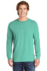 A smiling young man in a Comfort Colors Heavyweight Ring Spun Long Sleeve T-Shirt 6014 light teal and blue jeans stands against a plain white background.