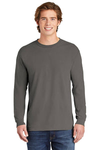 A young man with light brown hair stands and smiles at the camera against a white background, wearing a gray Comfort Colors Heavyweight Ring Spun Long Sleeve T-Shirt 6014 and blue jeans.