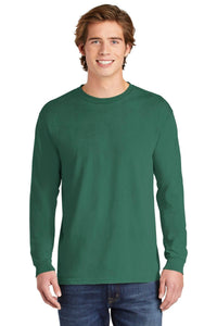 A young man stands facing forward, smiling, wearing blue jeans and a Comfort Colors Heavyweight Ring Spun Long Sleeve T-Shirt 6014 in forest green.