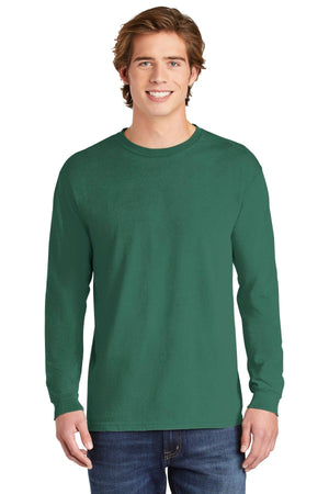 A young man stands facing forward, smiling, wearing blue jeans and a Comfort Colors Heavyweight Ring Spun Long Sleeve T-Shirt 6014 in forest green.