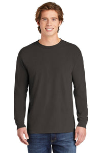 A young man smiles at the camera in a plain black Comfort Colors Heavyweight Ring Spun Long Sleeve T-Shirt 6014 and blue jeans, set against a white background.