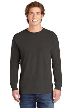 A young man smiles at the camera in a plain black Comfort Colors Heavyweight Ring Spun Long Sleeve T-Shirt 6014 and blue jeans, set against a white background.