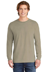 A young man smiles at the camera against a plain white background, wearing blue jeans and a Comfort Colors Heavyweight Ring Spun Long Sleeve T-Shirt 6014 in light olive green.