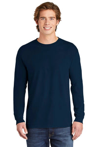 A young man smiles at the camera in blue jeans and a Comfort Colors Heavyweight Ring Spun Long Sleeve T-Shirt 6014 by Comfort Colors, standing against a white background.