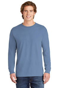 A young man smiles at the camera, wearing a Comfort Colors Heavyweight Ring Spun Long Sleeve T-Shirt 6014 in light blue and blue jeans, set against a white background.
