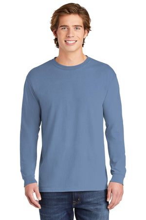 A young man smiles at the camera, wearing a Comfort Colors Heavyweight Ring Spun Long Sleeve T-Shirt 6014 in light blue and blue jeans, set against a white background.