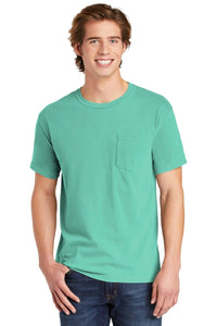 A young man with brown hair stands smiling at the camera, wearing blue jeans and a Comfort Colors Heavyweight Ring Spun Pocket T-Shirt 6030 in teal.