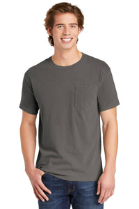 A young man smiles in a Comfort Colors Heavyweight Ring Spun Pocket T-Shirt 6030 in charcoal gray, paired with blue jeans, standing against a plain white background.