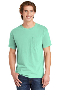 A young man, smiling with one hand in his jeans pocket, wears the Comfort Colors Heavyweight Ring Spun Pocket T-Shirt 6030 in mint green by Comfort Colors.