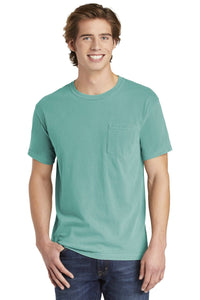A young man wearing a Comfort Colors Heavyweight Ring Spun Pocket T-Shirt 6030 in teal and blue jeans stands facing forward, smiling.
