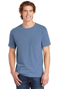 A young man wearing a Comfort Colors Heavyweight Ring Spun Pocket T-Shirt 6030 in light blue and blue jeans stands and smiles at the camera.