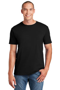 A person smiles in a black Gildan Softstyle T-Shirt 64000, made of ring spun cotton, and blue jeans, stands with one hand in their pocket against a white background. The modern classic fit by Gildan enhances their style while ensuring comfort.