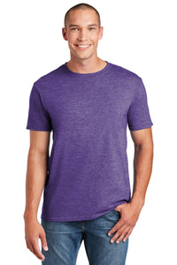 A person wearing a Gildan Softstyle T-Shirt 64000 in purple with a modern classic fit and blue jeans, standing and smiling against a white background.