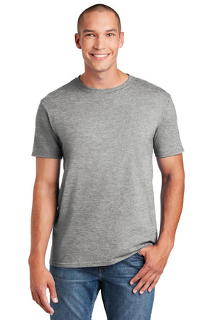 A smiling person in a Gildan Softstyle T-Shirt 64000, made of ring spun cotton with a modern classic fit, stands in jeans with one hand in their pocket against a white background.