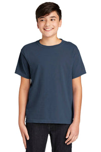 A smiling boy in a Comfort Colors Youth Ring Spun T-Shirt 9018 and black pants stands against a white background.
